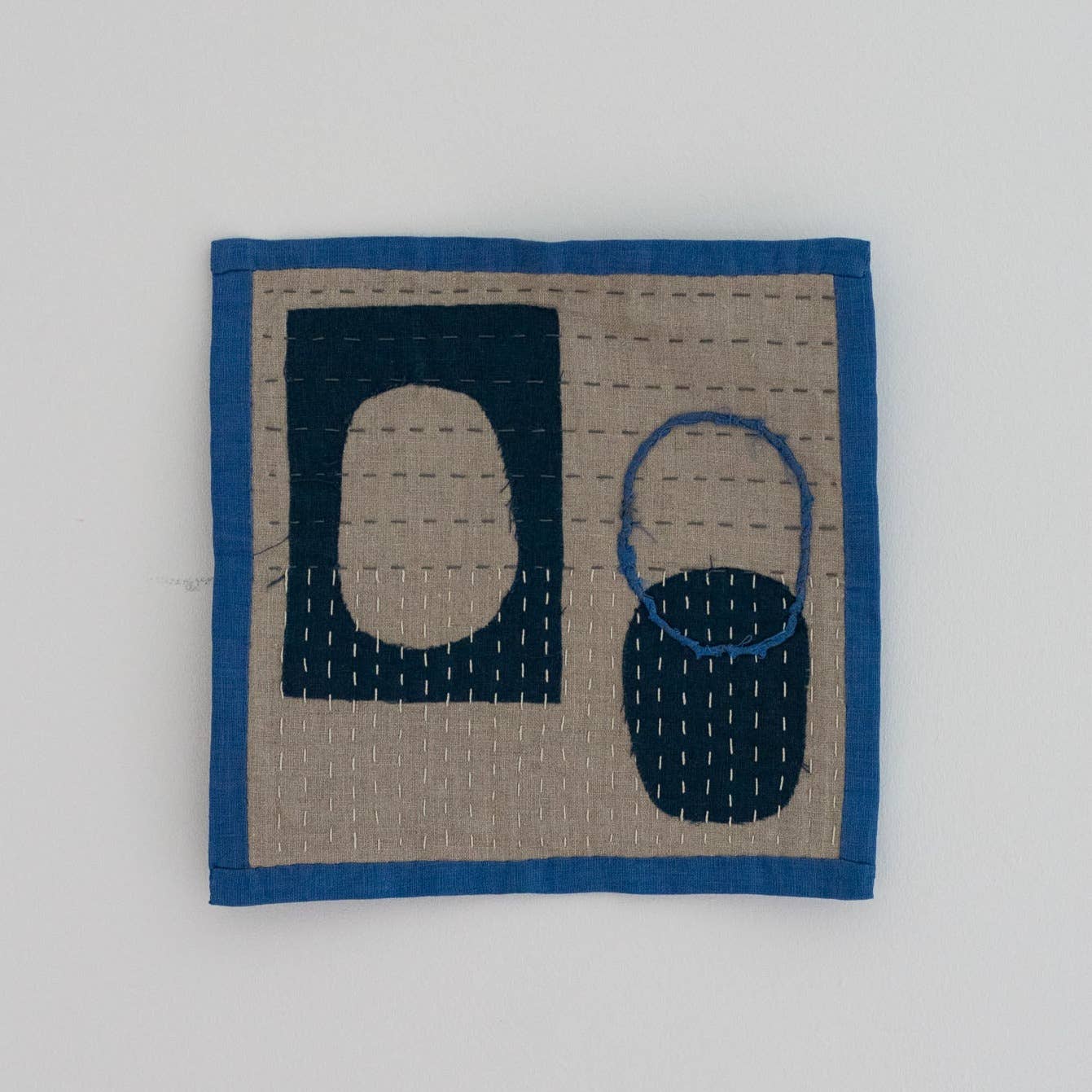 Square quilt with blue border featuring abstract shapes on a light gray background