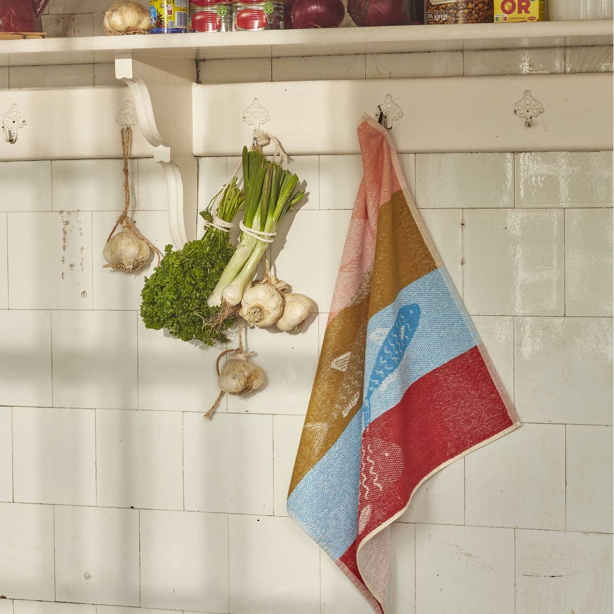 Colourful towel with fish design hanging on a hook with vegetables on a tiled wall