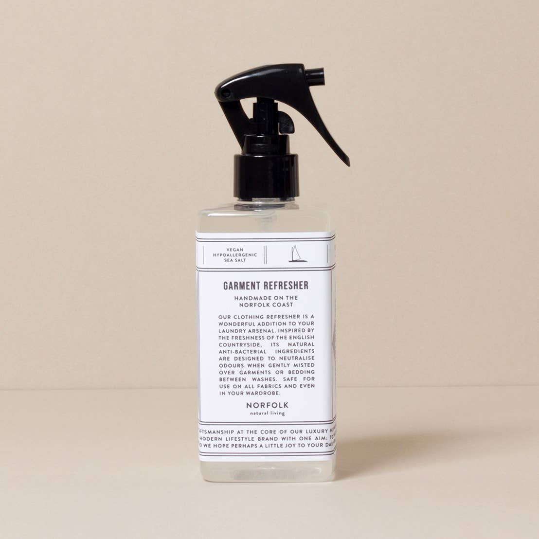 Clear spray bottle with black nozzle on a beige background
