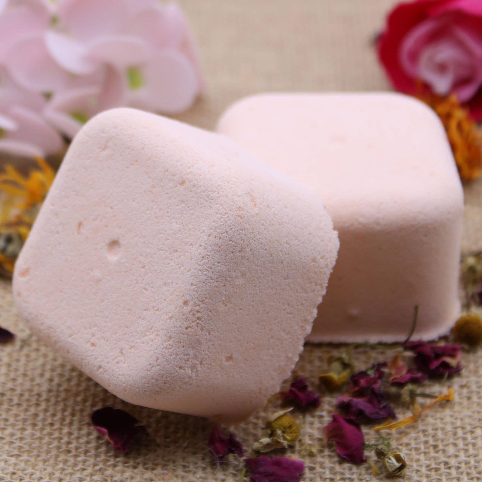 Two pink bath bombs on a textured surface with flowers and petals.