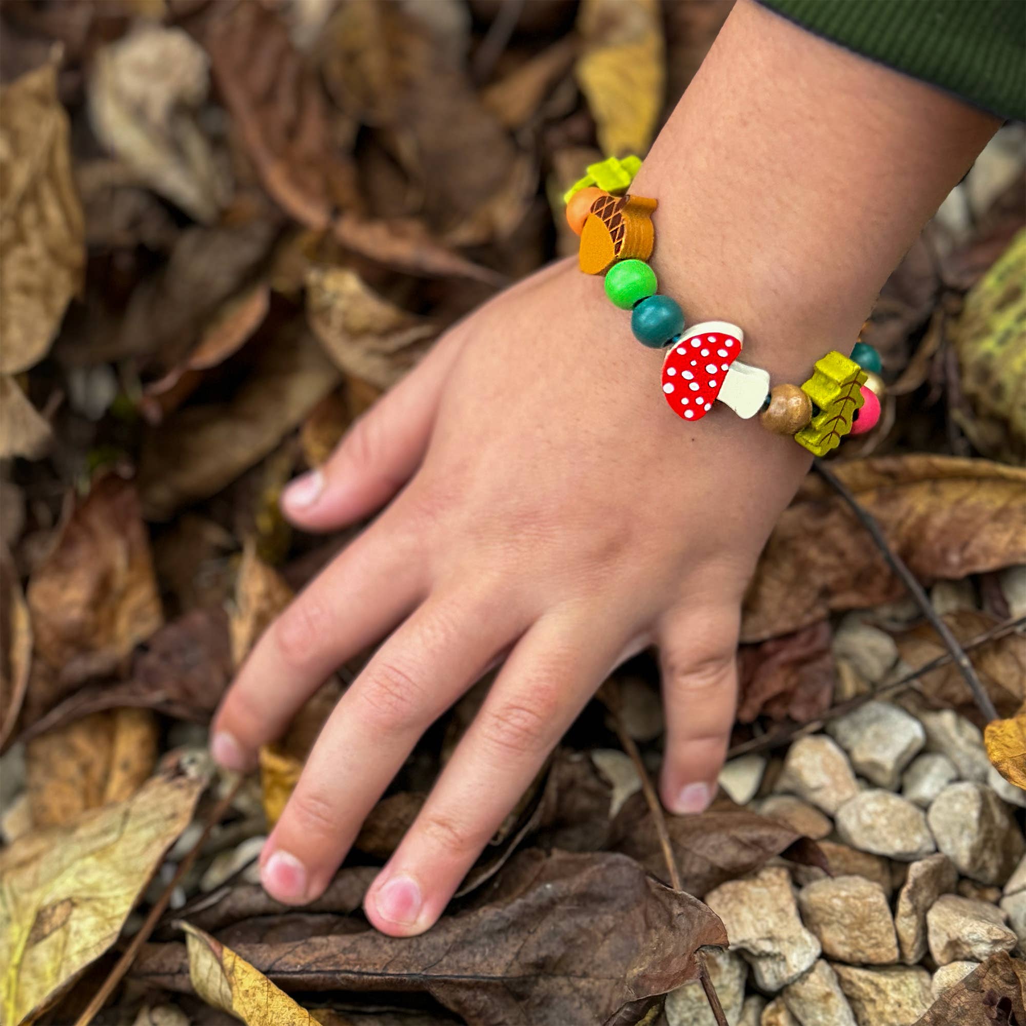 Child's hand wearing a colorful beaded bracelet on a leafy ground