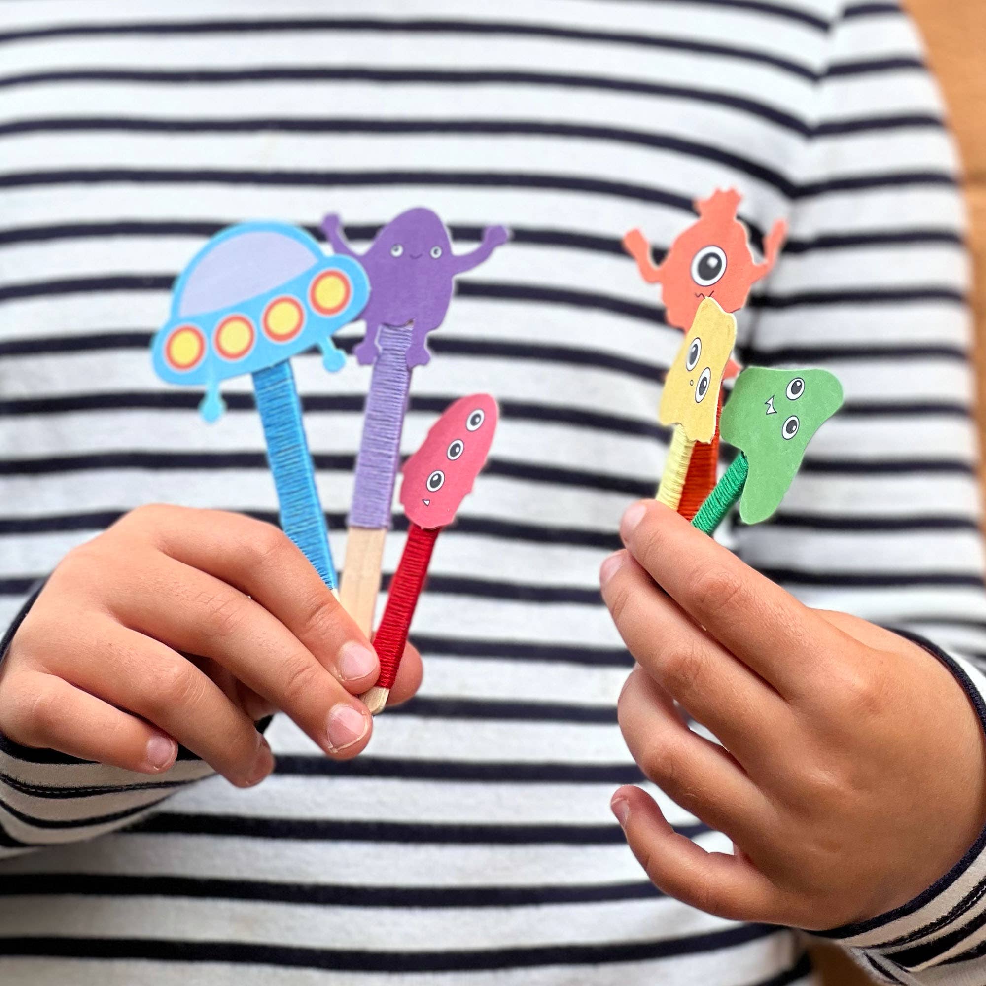Colorful alien-shaped pens held by a child against a striped shirt background