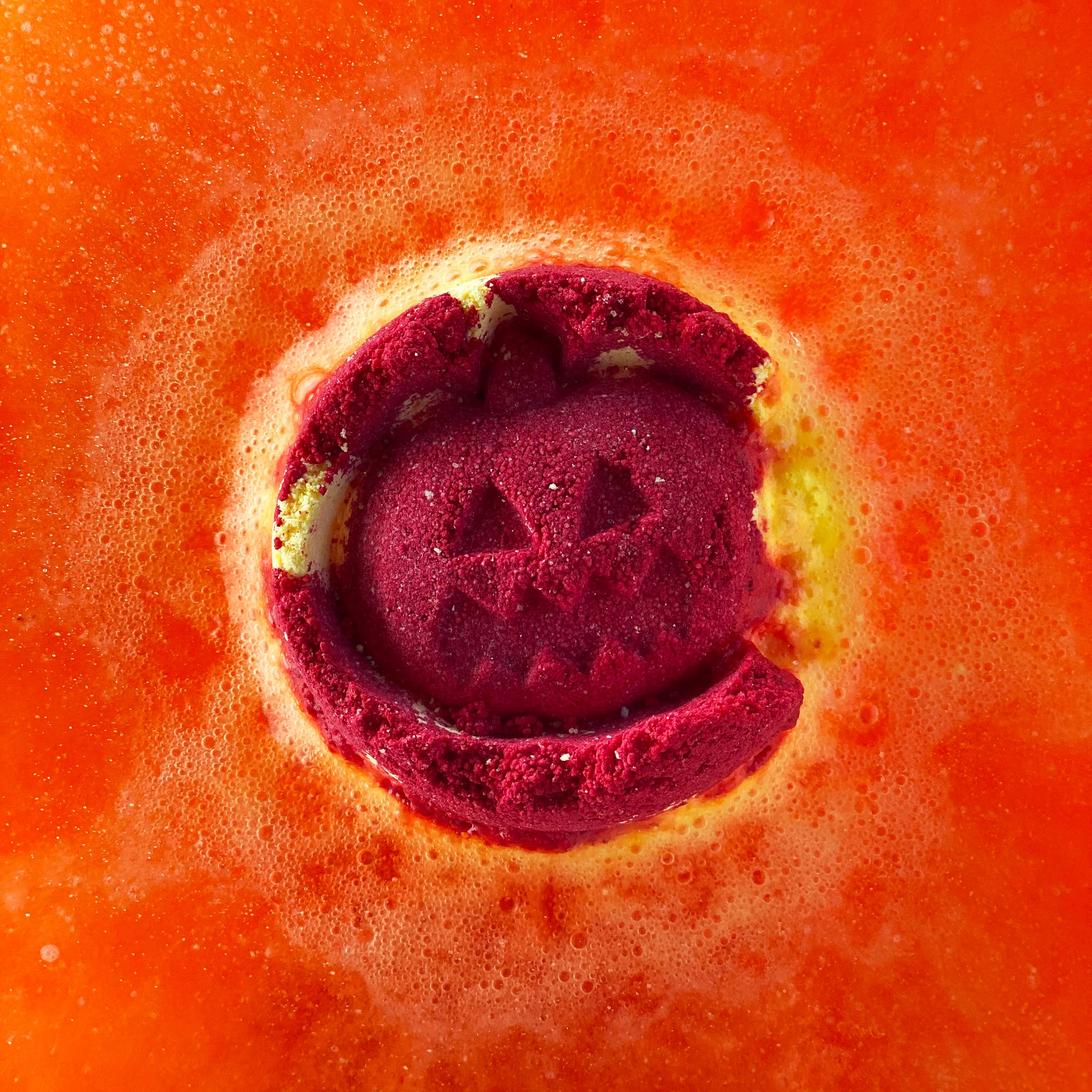Red bath bomb with a pumpkin design on an orange background