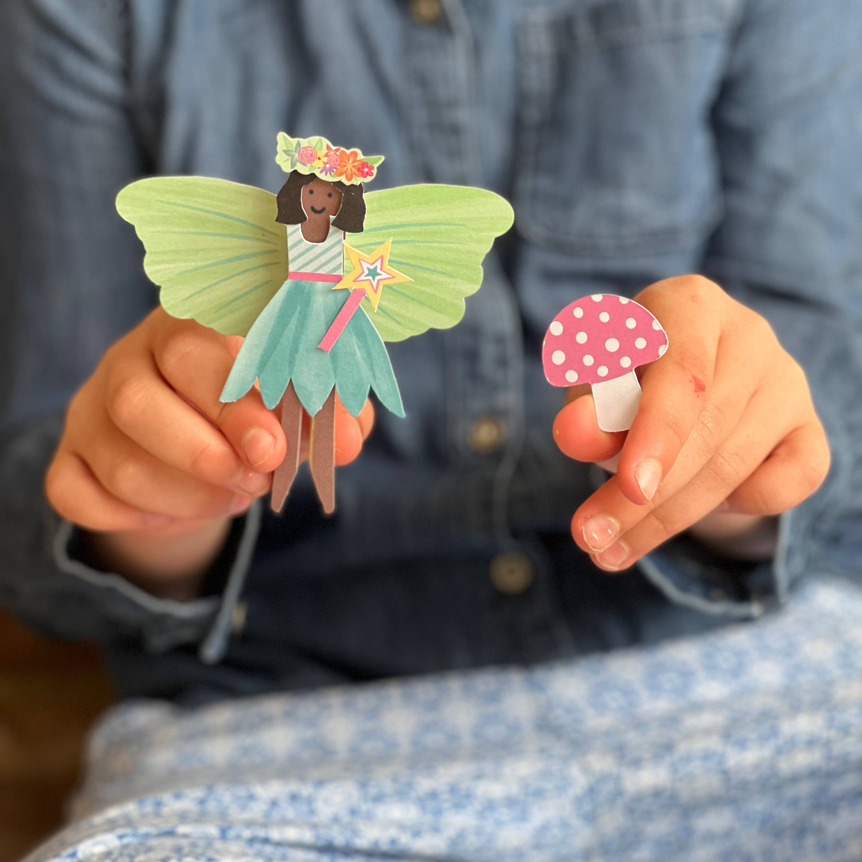 Child holding a paper fairy and mushroom toy