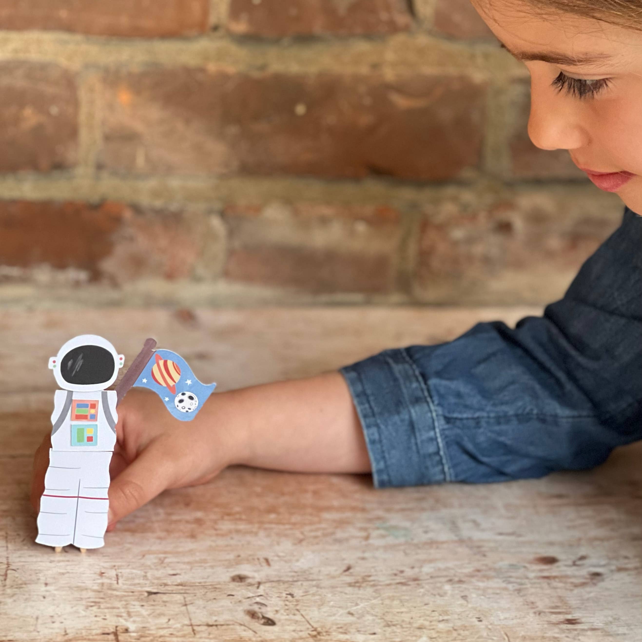 Child holding a paper astronaut and flag against a brick wall background
