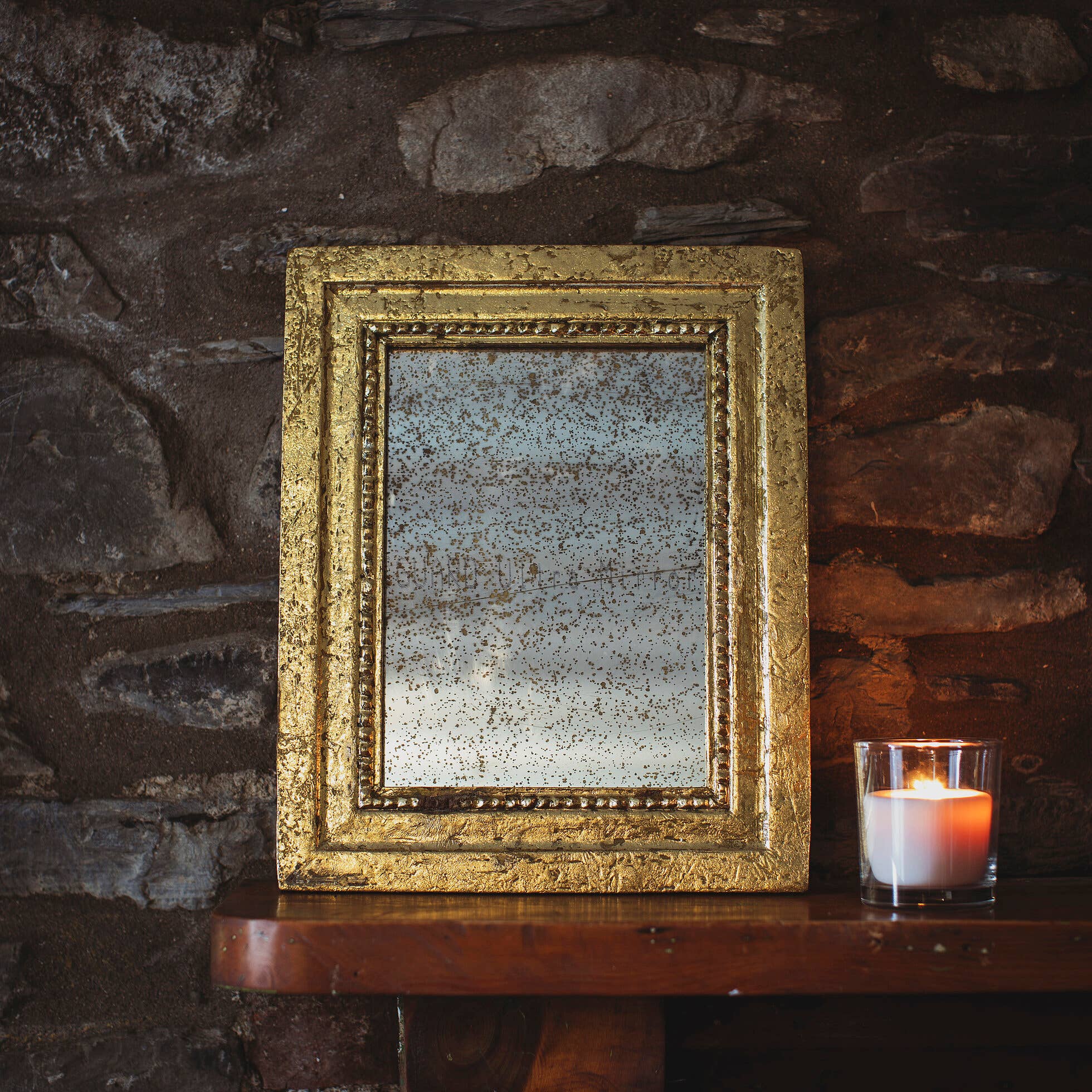 Gold-framed mirror on a stone wall with a candle beside it