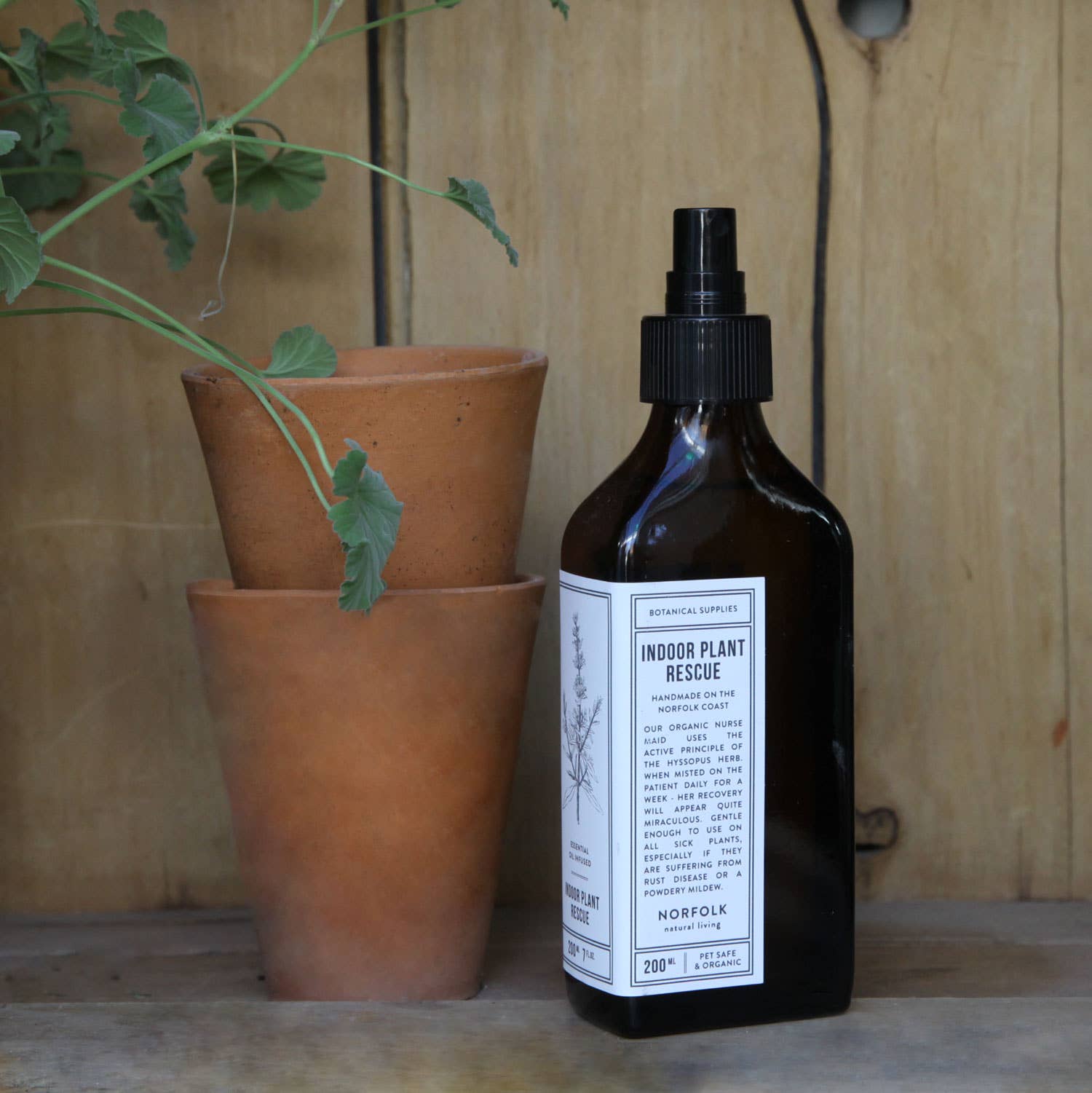 Bottle of indoor plant rescue spray next to terracotta pots on a wooden surface
