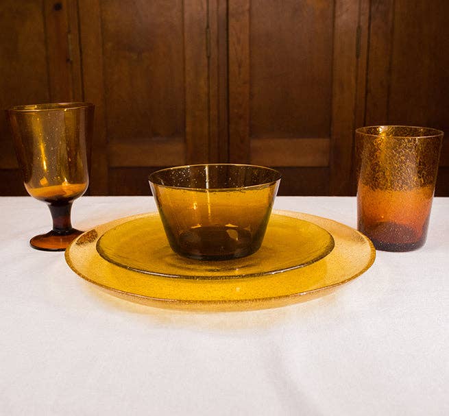 Set of amber glass tableware including a bowl, plates, and glasses on a white surface with wooden background.