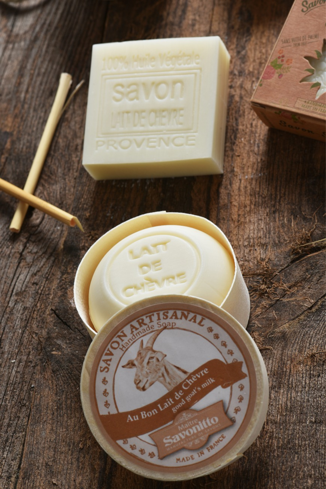 Bar of soap and container on a wooden surface with Savon Artisanal labels.