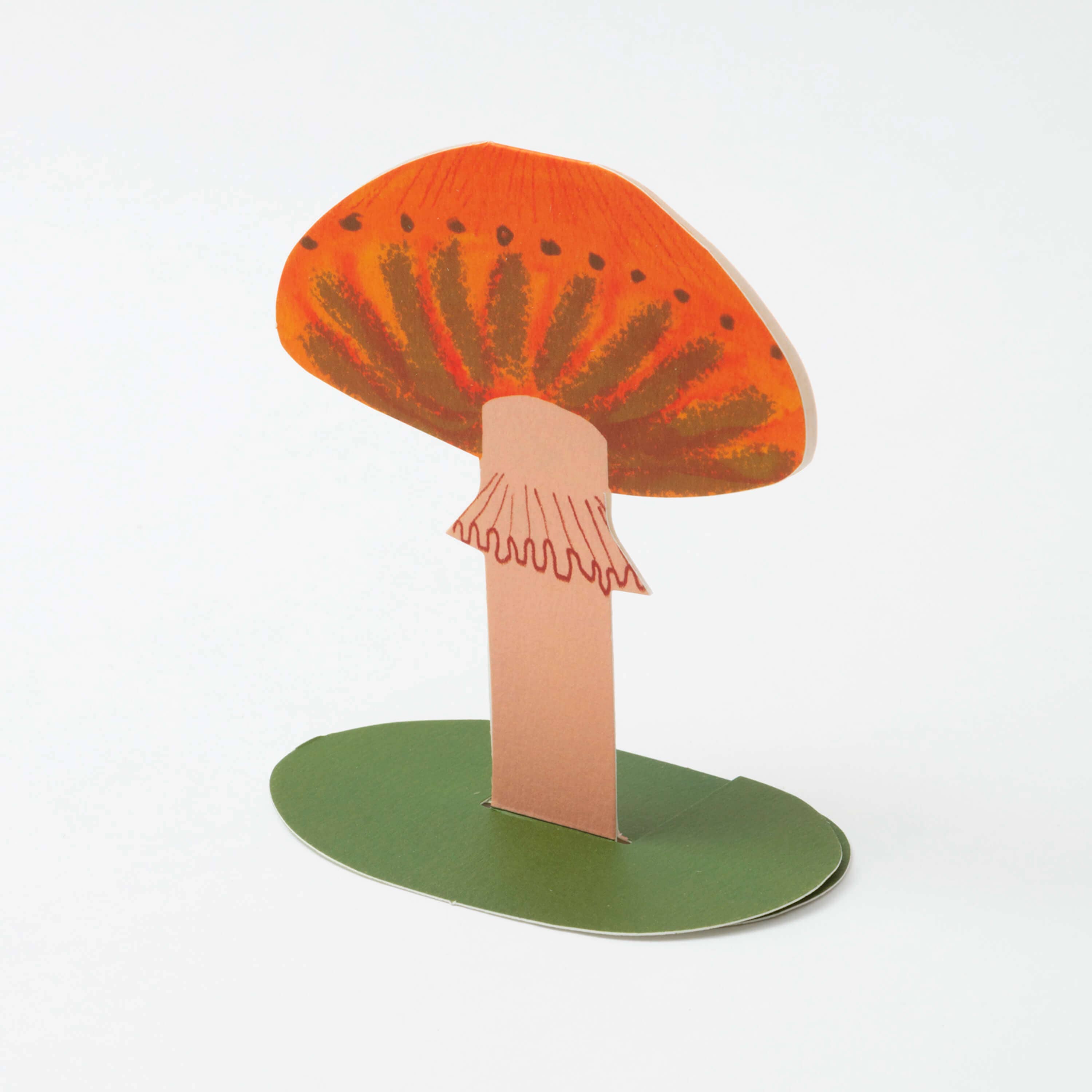 Cardboard cutout of a mushroom with an orange cap and green base on a white background