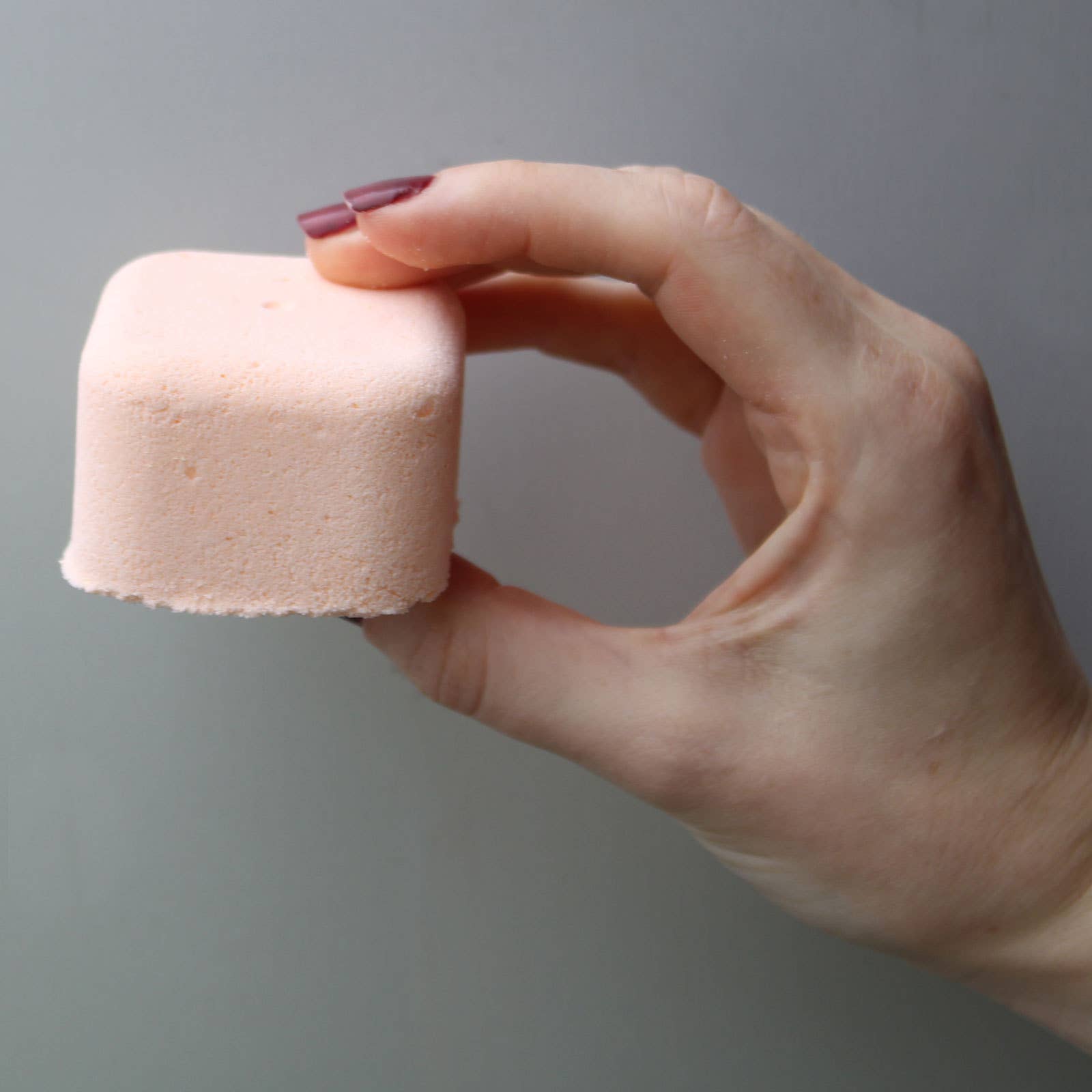 Hand holding a pink bathbomb against a gray background