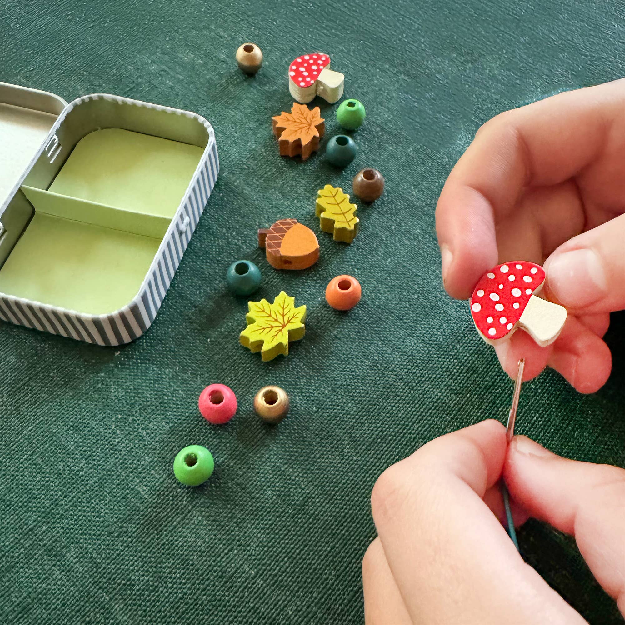 Colorful mushroom-shaped beads being held by a hand on a green surface with more beads scattered around.