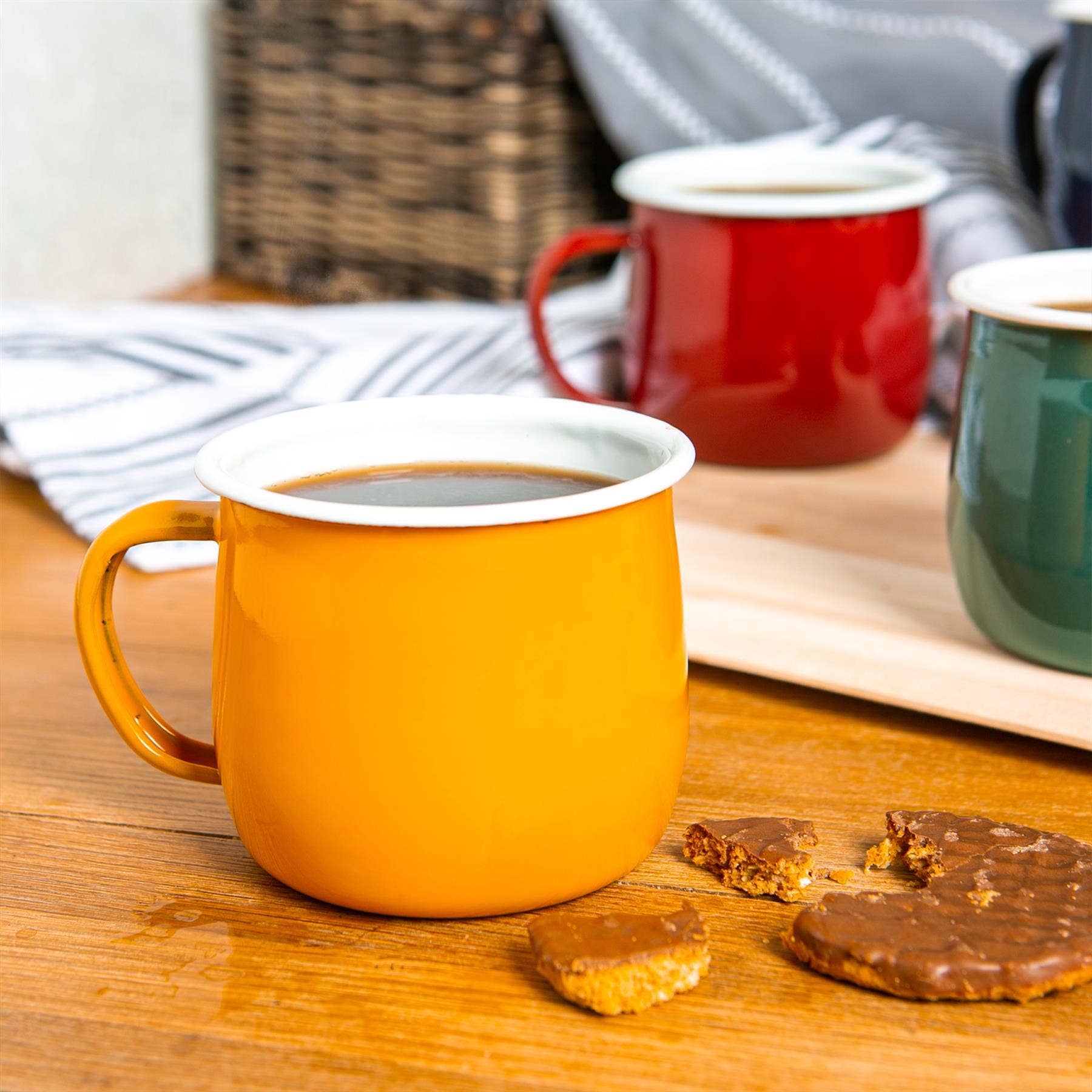 Orange mug with a white interior on a wooden surface with cookies and other mugs in the background.