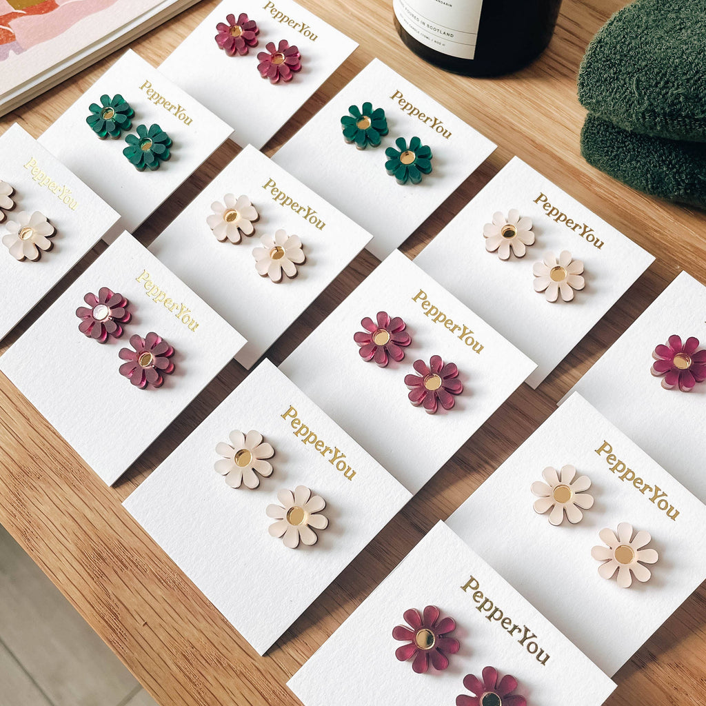 Set of floral earrings on branded cards with a wooden surface background.