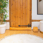 Decorative setting with yellow cylindrical pillow, white rug, and wooden wall.