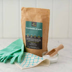Bag of bicarbonate of soda with gloves, cloth, and scoop on a light surface