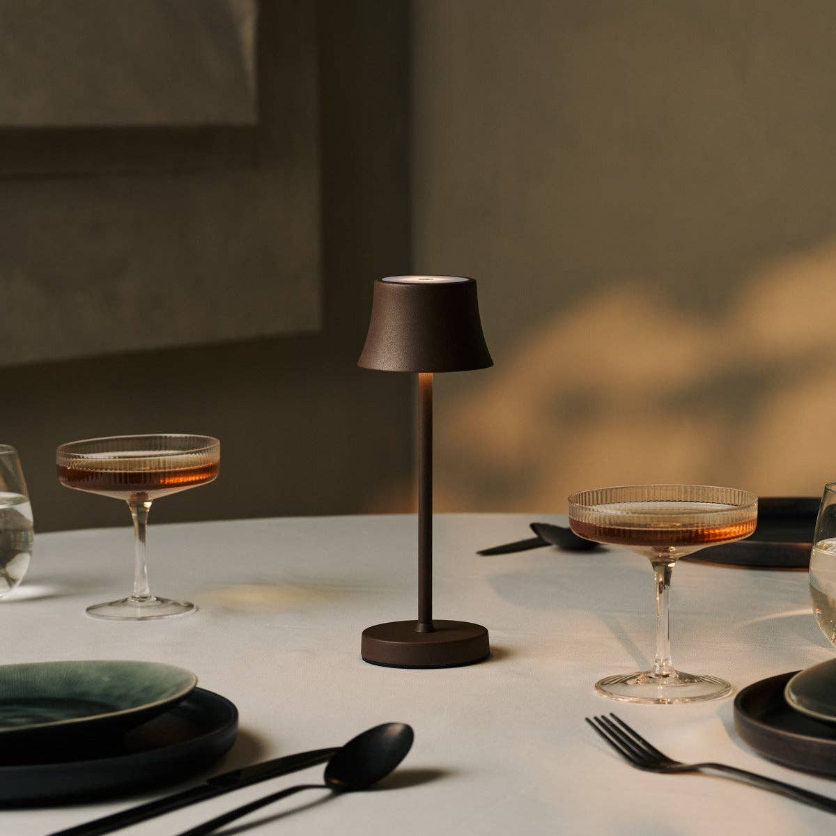 Table setting with a lamp, glasses, and plates on a neutral background