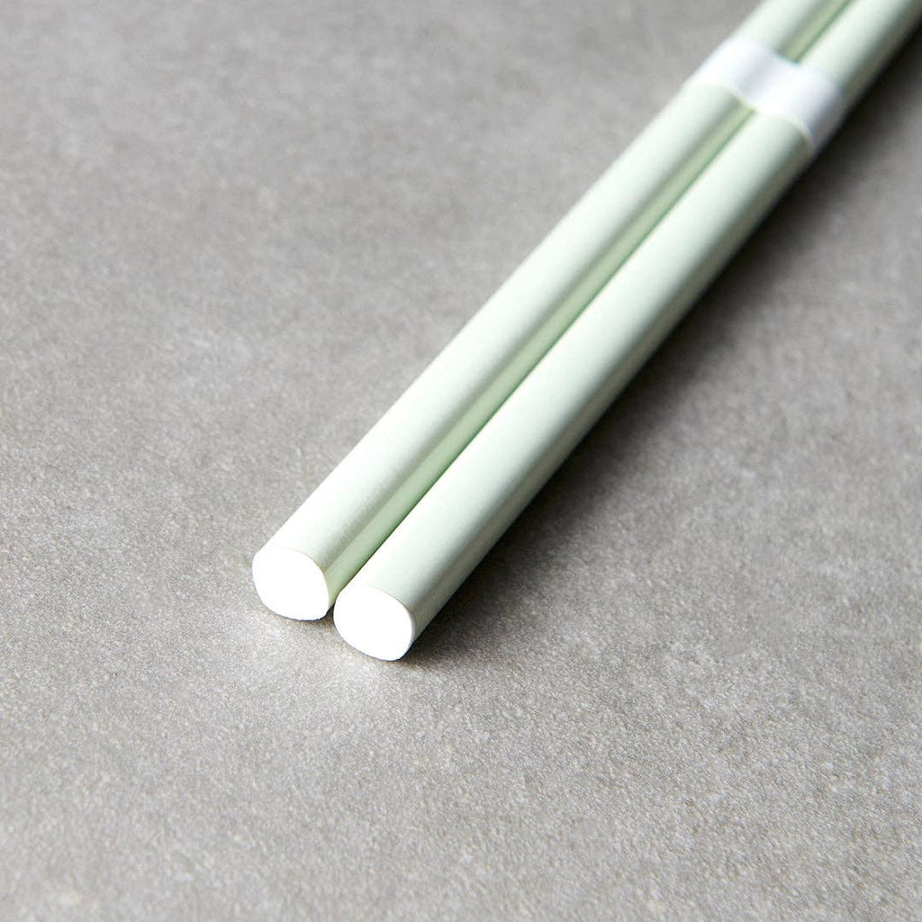 Two light green chopsticks on a gray surface