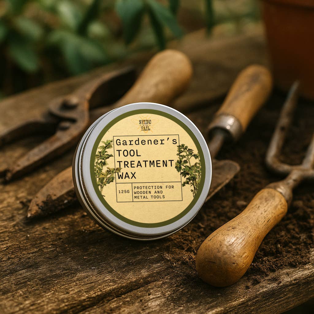 A tin of Gardener's Tool Treatment Wax surrounded by old fashioned gardening tools on a wooden surface