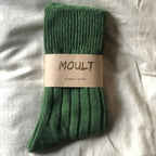 Green alpaca sock with 'MOULT' label on a light fabric background