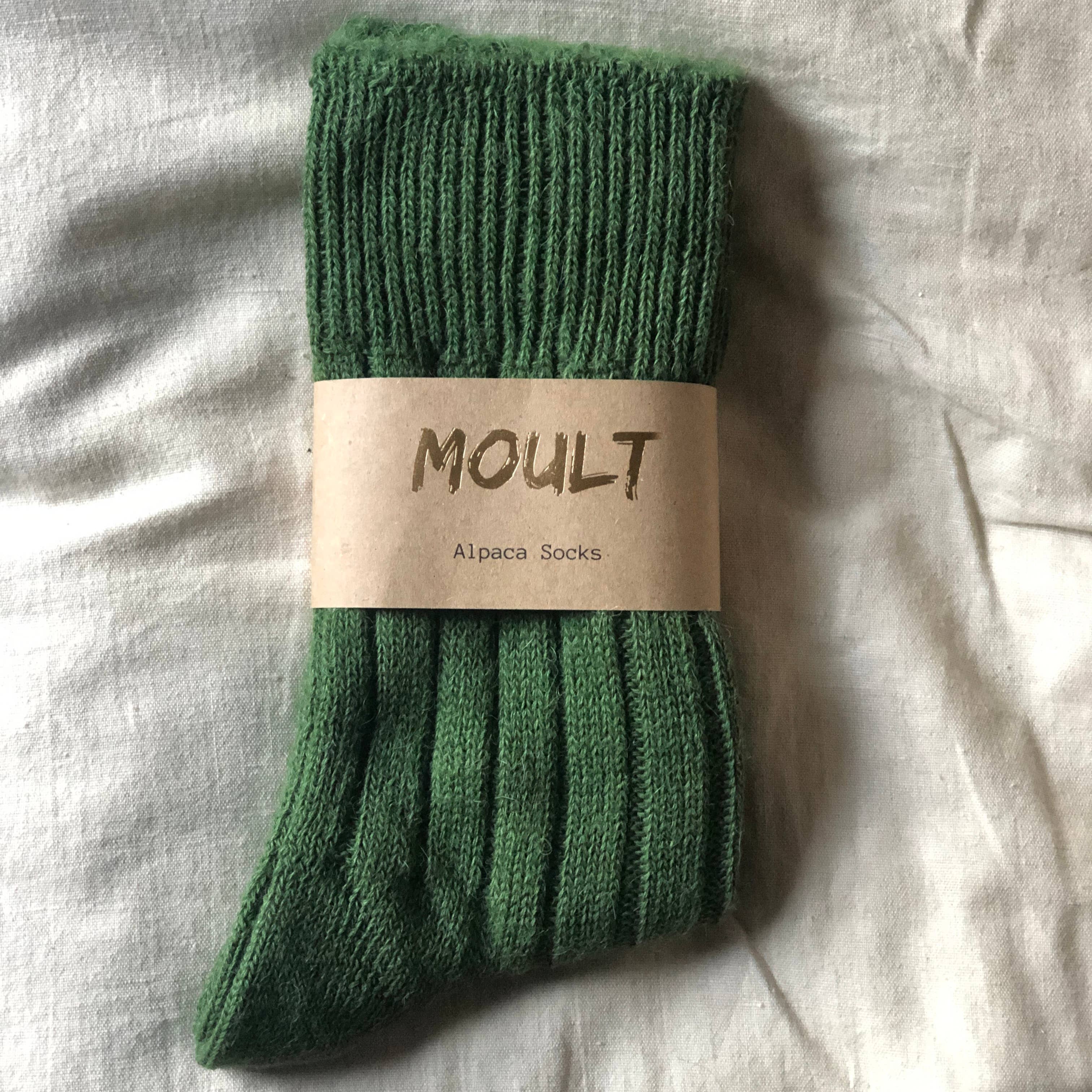 Green alpaca sock with 'MOULT' label on a light fabric background