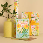 Floral-themed greeting cards and gift wrap with a yellow vase on a beige background