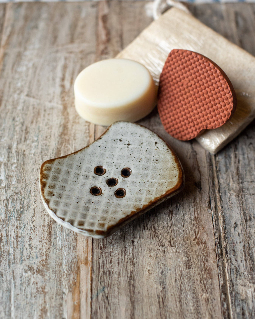 Bar of soap, scrubber, and soap dish on a wooden surface