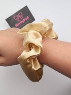 Gold scrunchie on a wrist with a branded card in the background