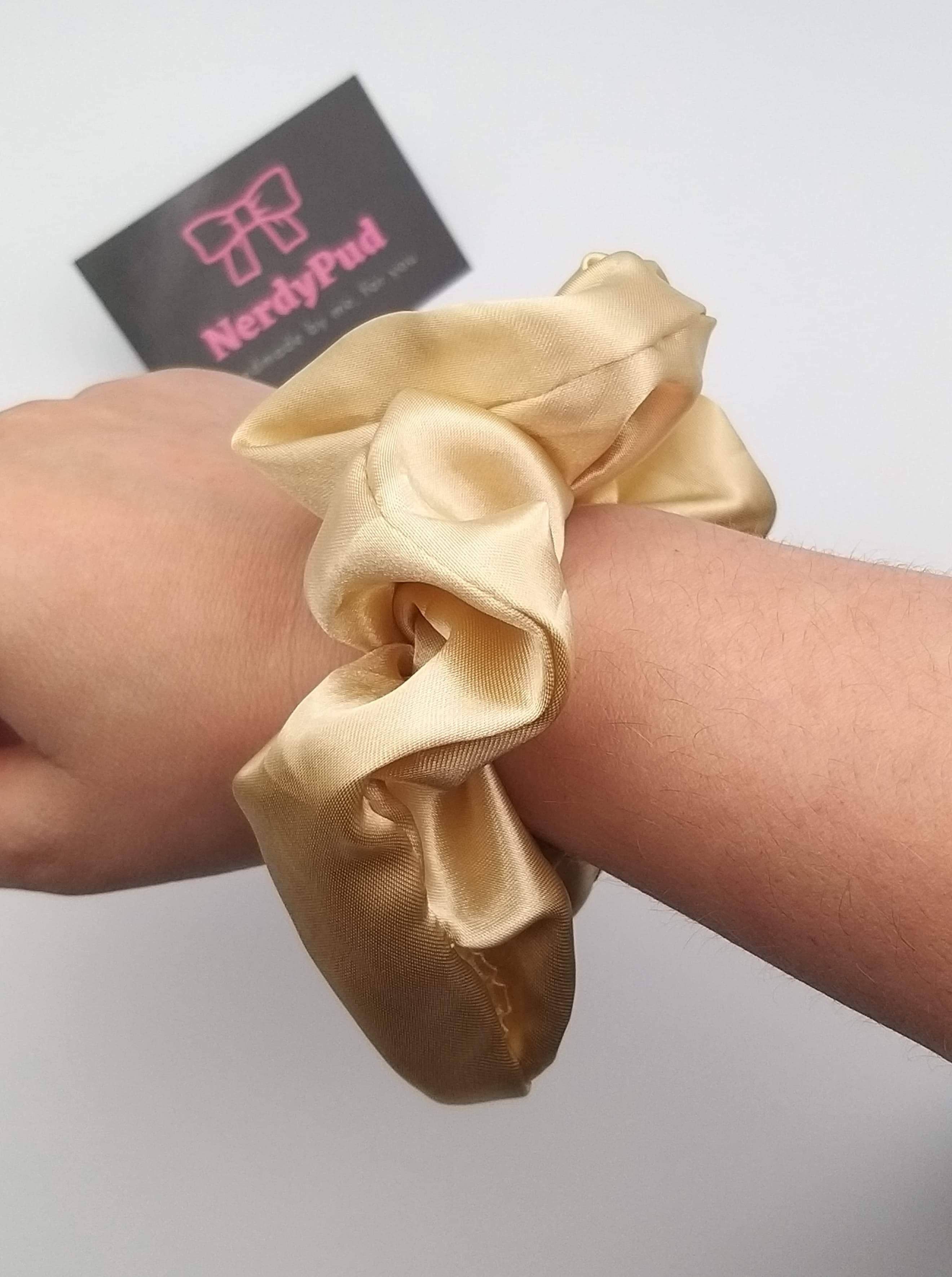 Gold scrunchie on a wrist with a branded card in the background