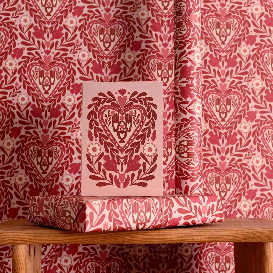 Pink decorative box with heart design on a wooden surface against a red and white patterned curtain.