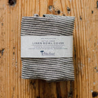 Folded black and white striped linen bowl cover with a label on a wooden surface