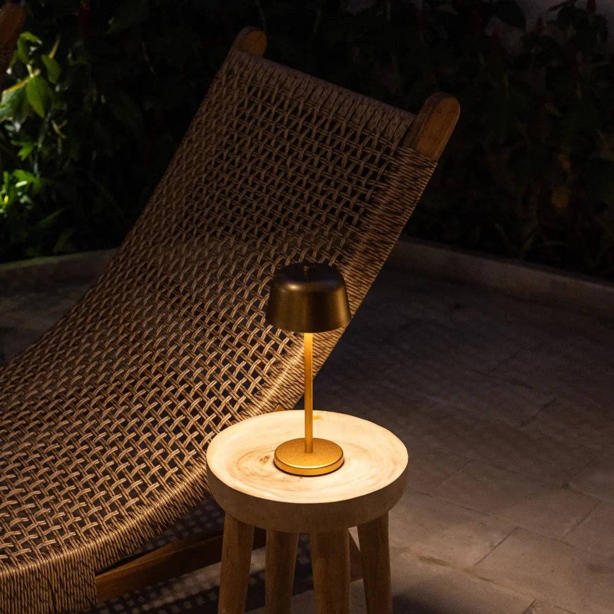 Small table lamp on a wooden stool next to a wicker chair outdoors.