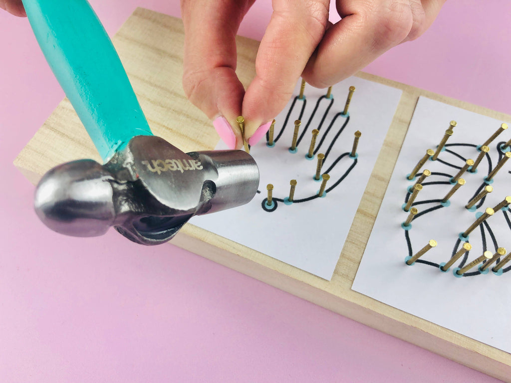 Hand using a hammer to bend metal wires on a pink background