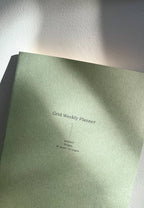Green planner with 'Grid Weekly Planner' text on a white surface