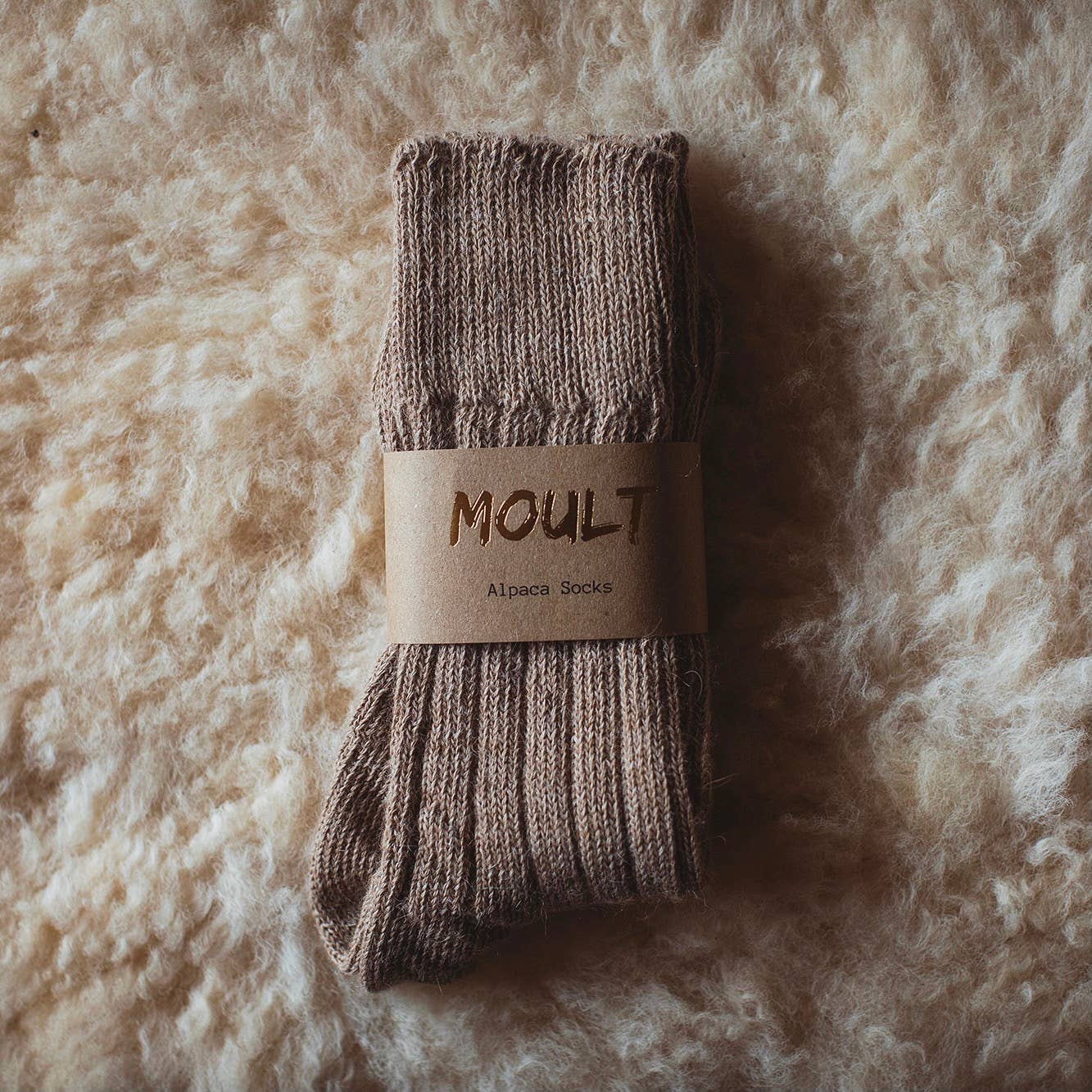 Pair of brown socks with a 'Moul't' label on a textured beige background