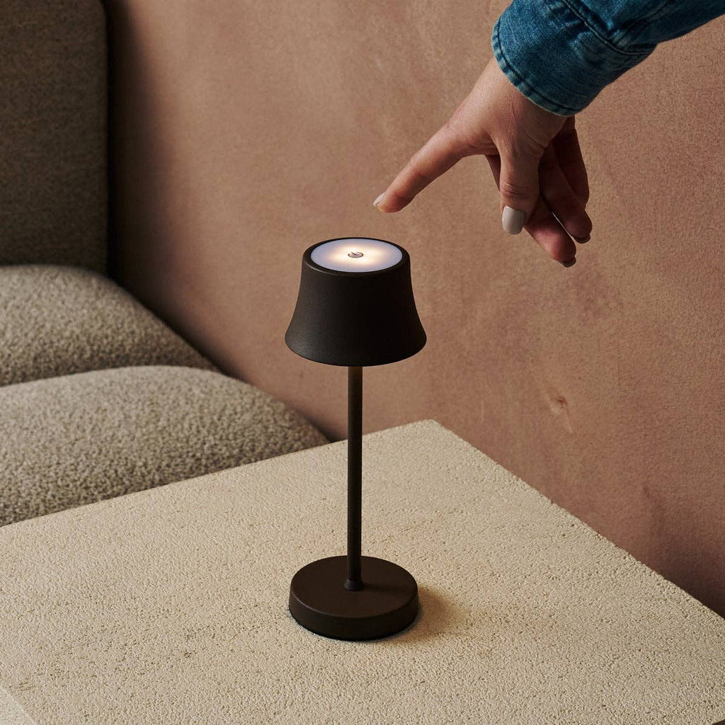 Person interacting with a small black lamp on a beige surface.