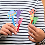 Colorful alien-shaped pens held by a child against a striped shirt background