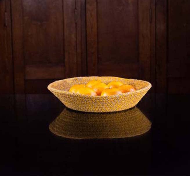 Woven basket with oranges on a reflective surface in front of a wooden panel.