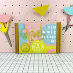 Gold Wire Jig Earrings Kit packaging on a pegboard background with crafting tools.