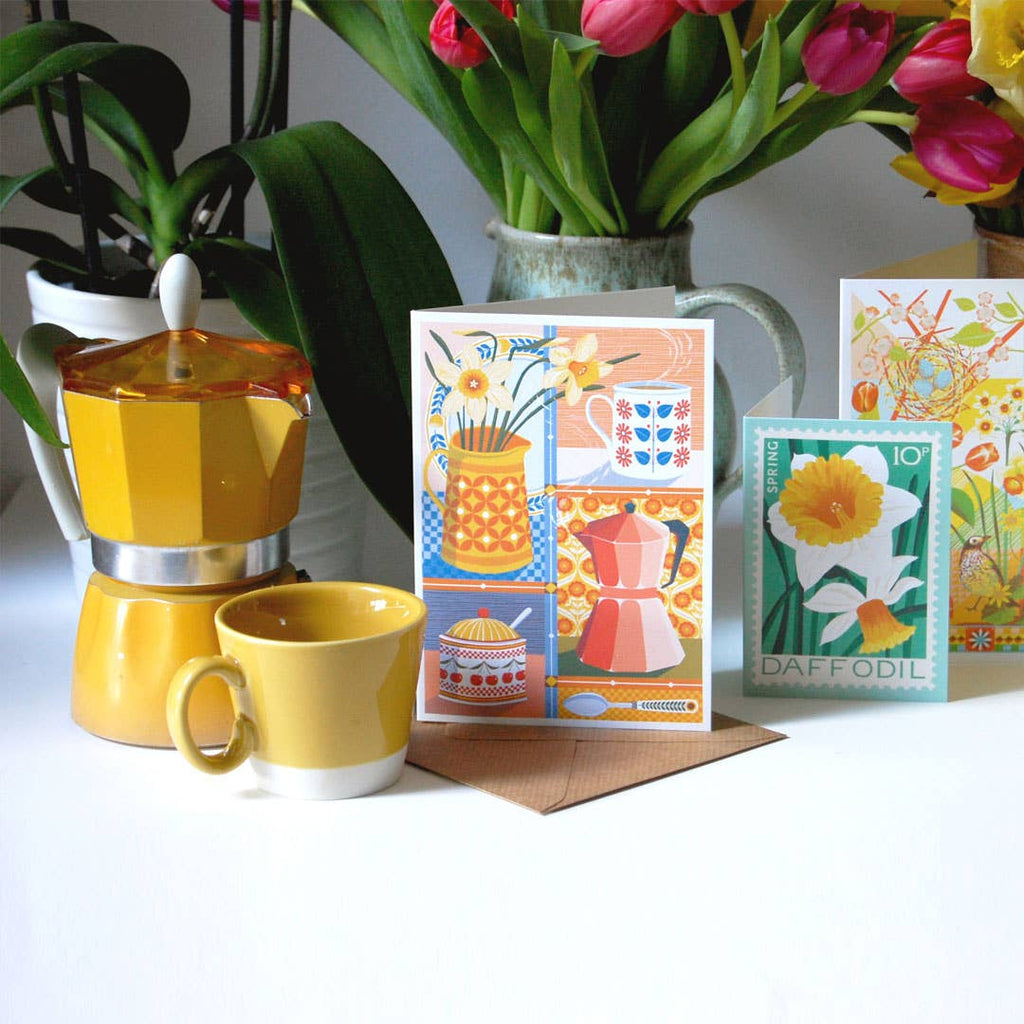 Yellow coffee maker and mug with floral cards on a white surface