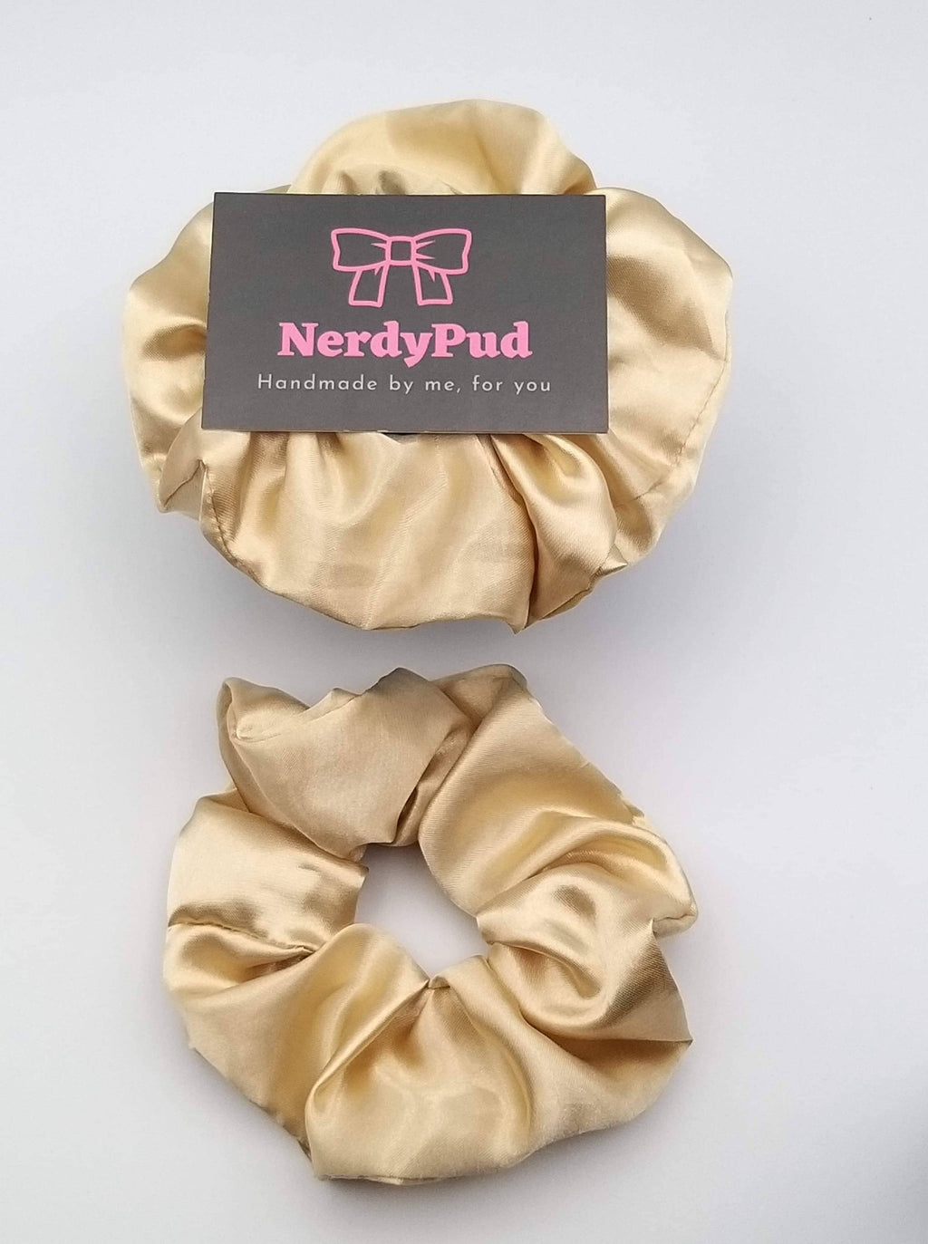 Two gold scrunchies with a 'NerdyPud' branded card on a light gray background