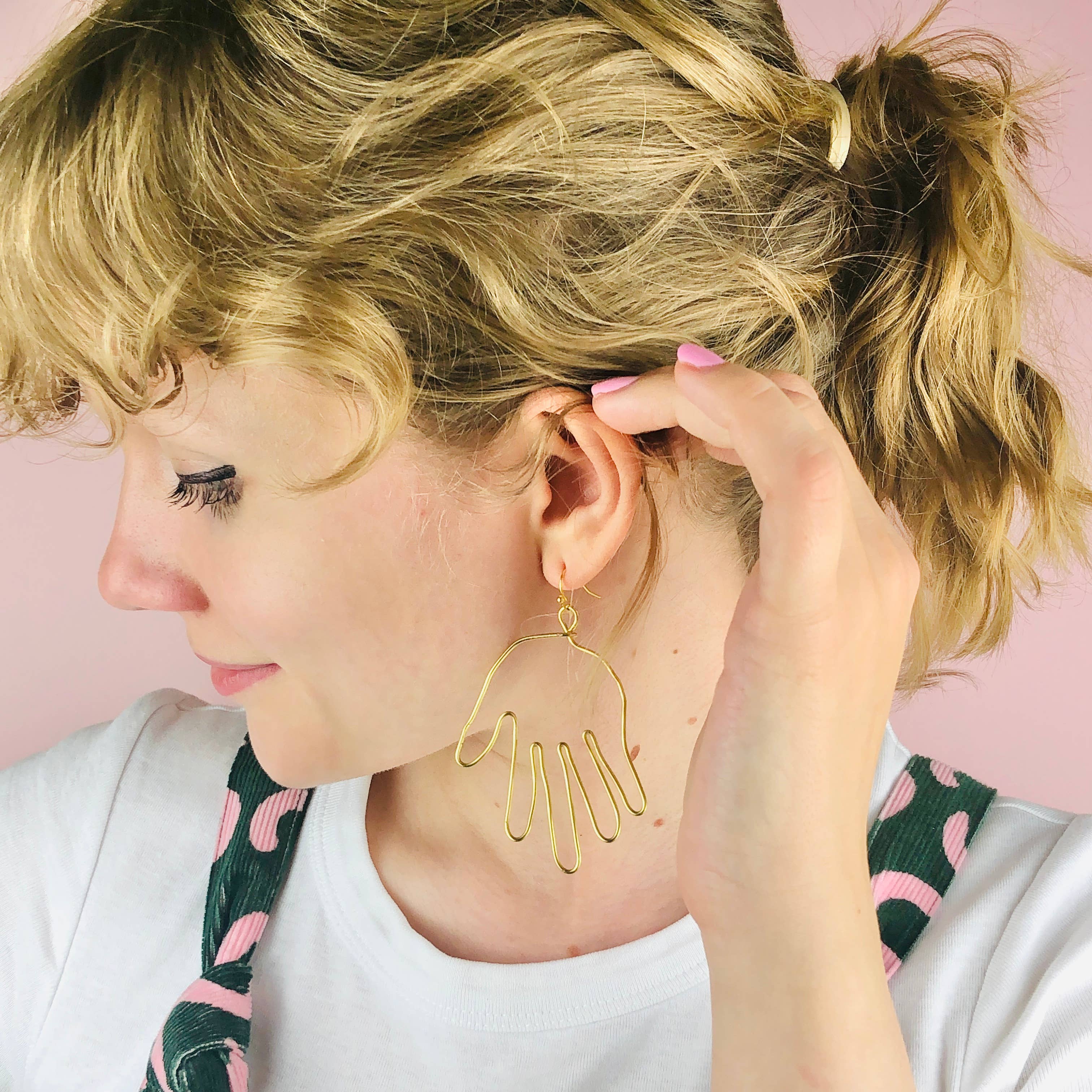 Woman wearing gold earrings with a pink background