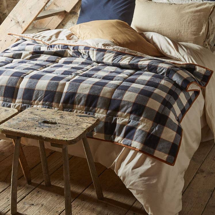 Checkered quilt on a bed with wooden floor and stool