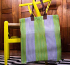 Striped green and blue bag hanging on a yellow chair with a wooden wall background