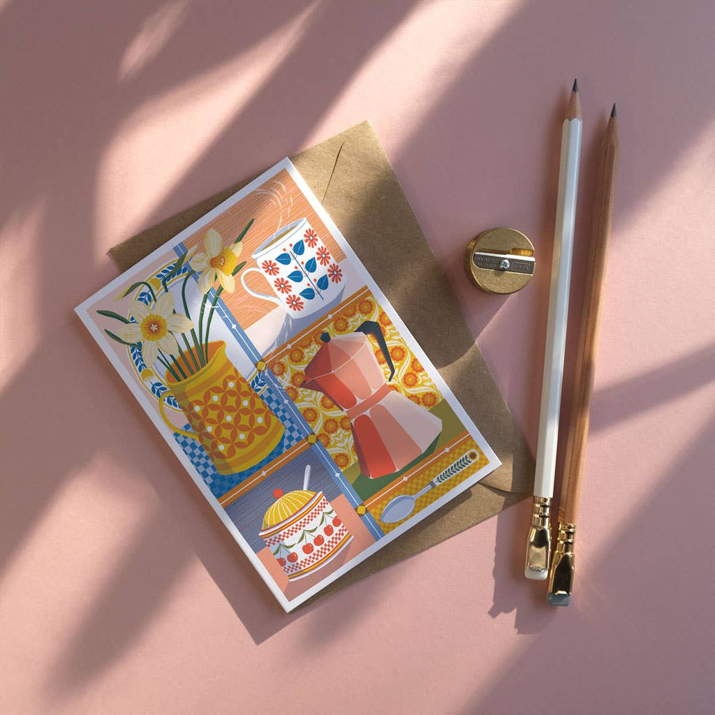 Greeting card with colorful illustrations of kitchen items on a pink surface with a pencil and sharpener.