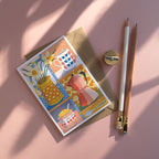 Greeting card with colorful illustrations of kitchen items on a pink surface with a pencil and sharpener.