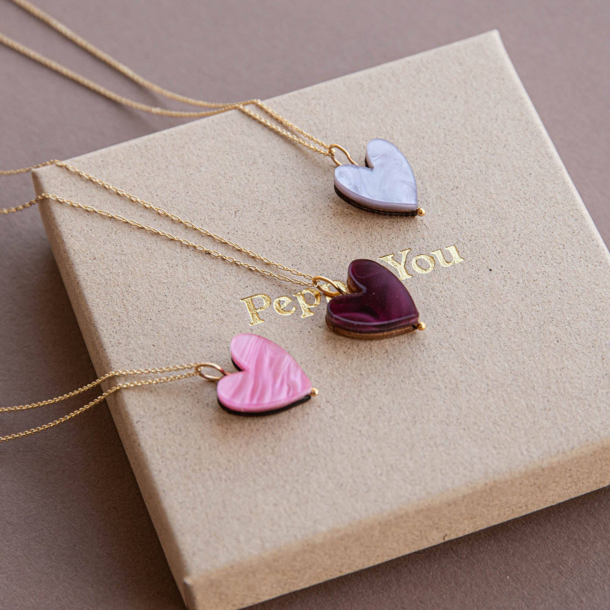 Heart-shaped pendants on gold necklaces on a beige box.