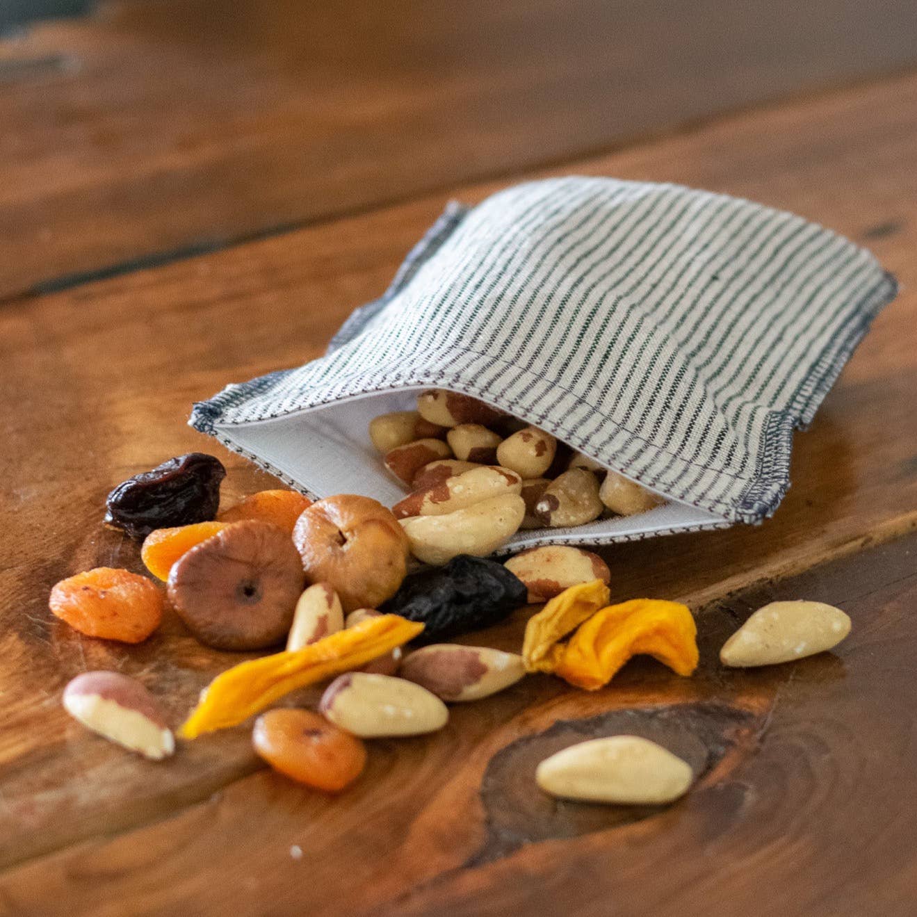 Assorted dried fruits and nuts spilling out of a striped fabric bag on a wooden surface.