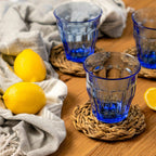 Blue glass tumblers on woven coasters with lemons on a wooden surface