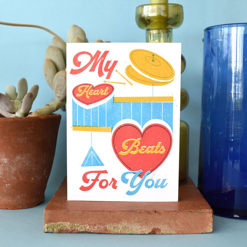 Card with 'My Heart Beats For You' text and heart design on a stand with decorative items in the background.